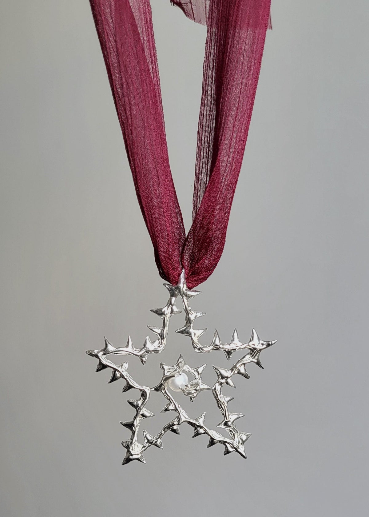 Silver star-shaped ornament on a red ribbon against a gray background