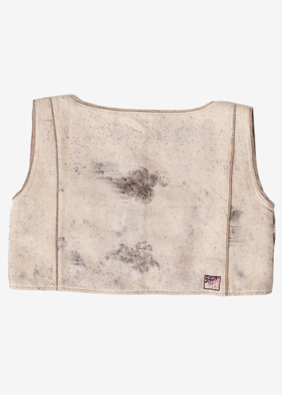 The back of a cropped sleeveless vest in a distressed, washed beige fabric with dark gray and brown mottled stains, shown on a plain white background.
