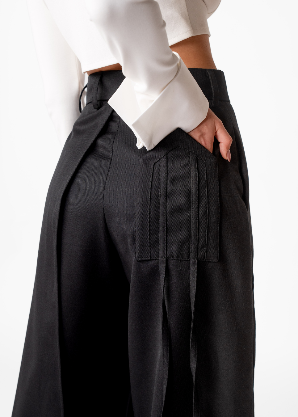 Close-up of a person wearing black wide-leg pleated trousers with a white cropped top, shown against a plain light background.