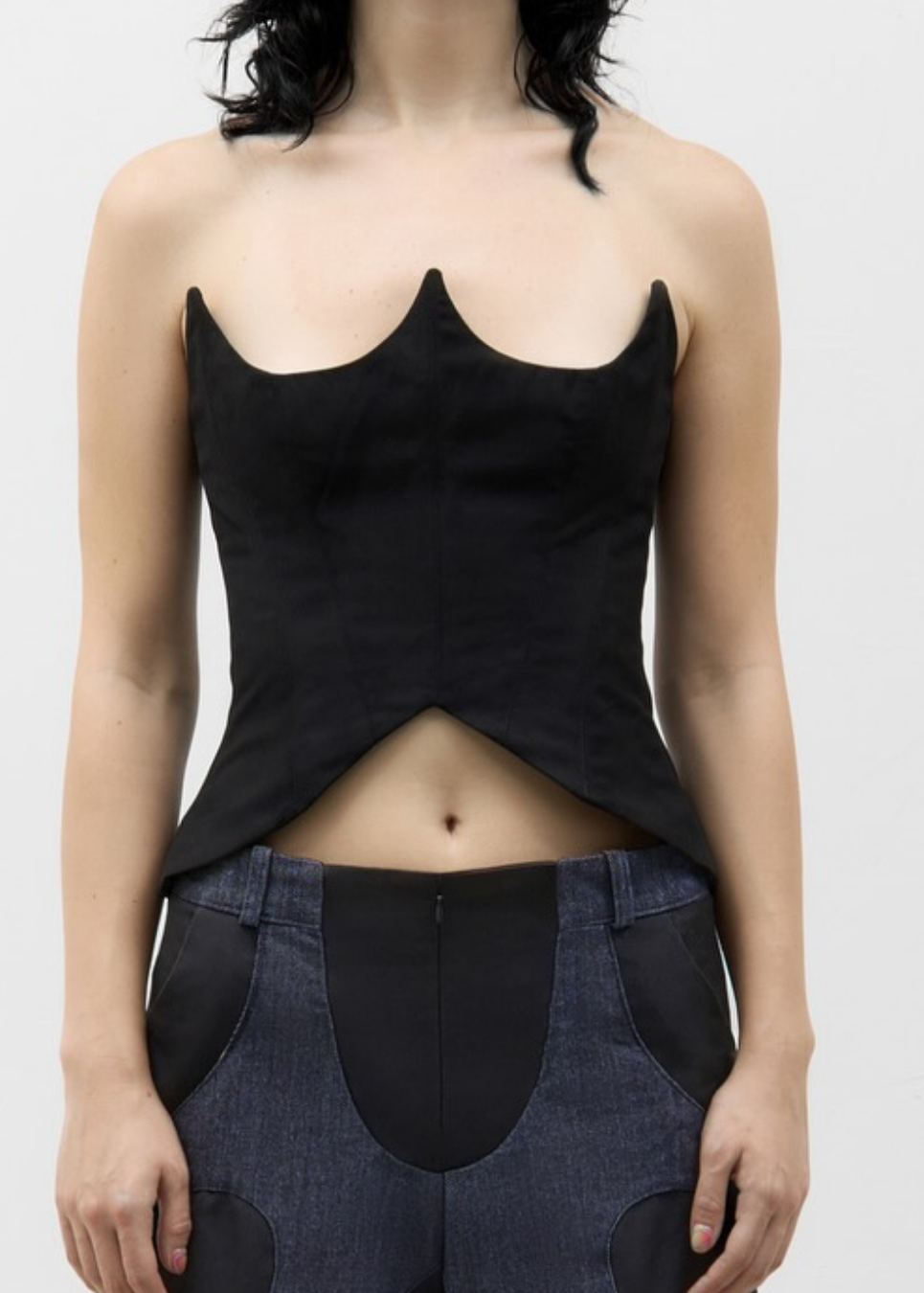 Person wearing a black sleeveless top and dark blue overalls on a white background