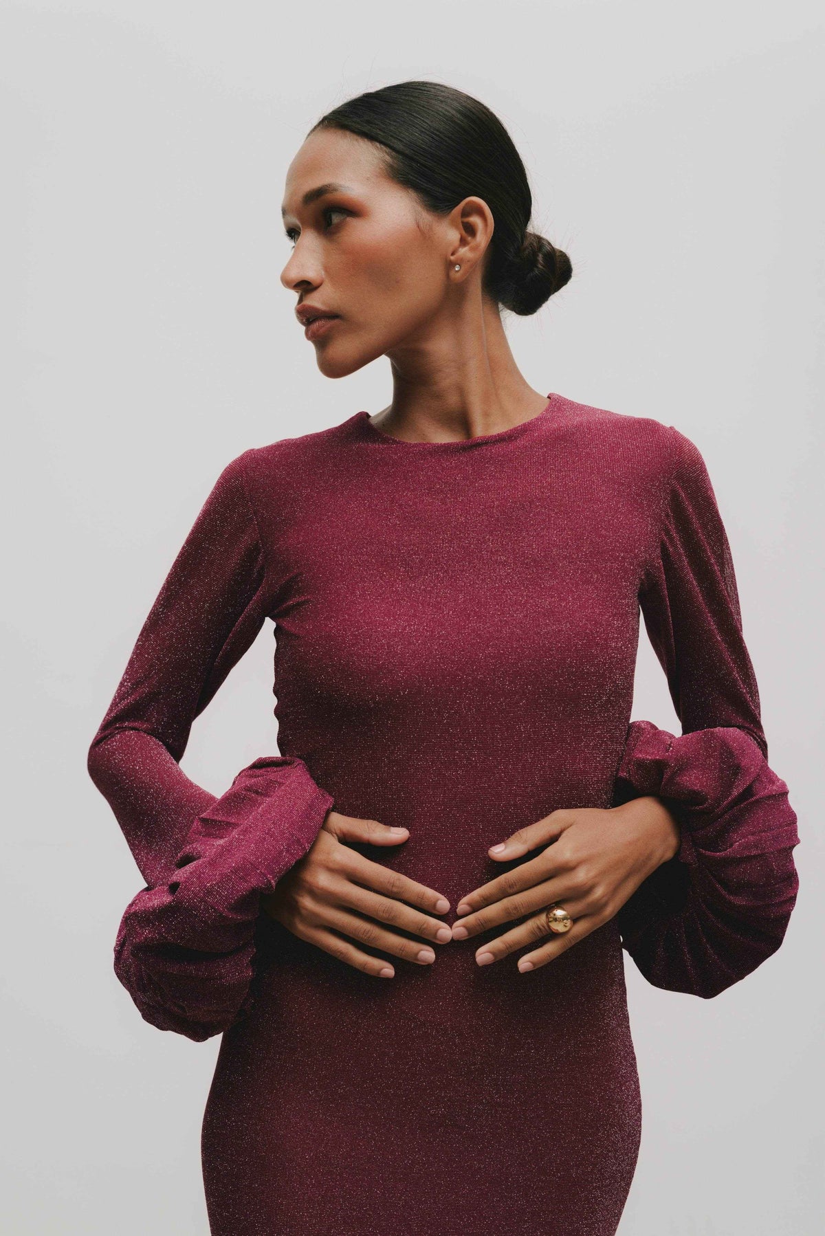 A model wearing a long red wine colored dress with pleated sleeves and a slit at the thighs.