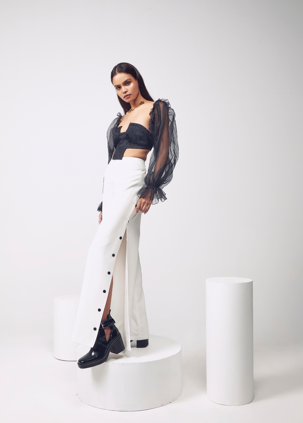 Woman in black crop top and white pants with sheer sleeves on a white background
