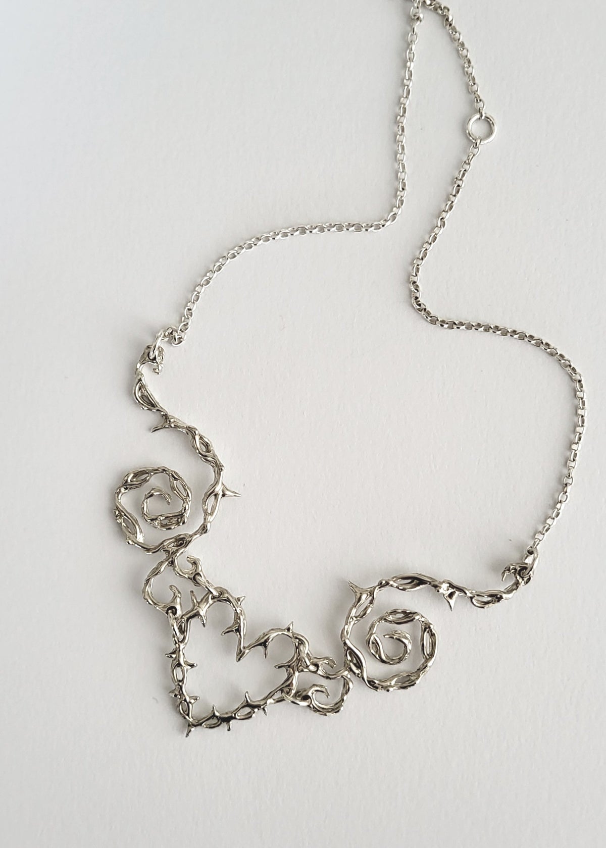 Silver necklace with decorative pendants on a light gray background