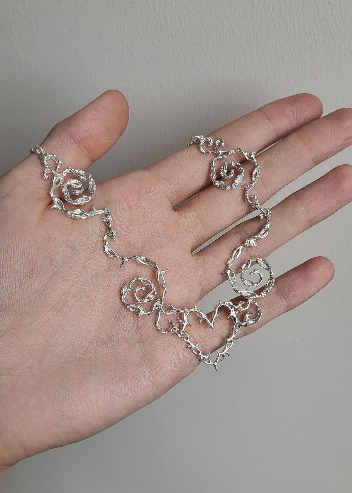 Silver necklace on a hand against a neutral background