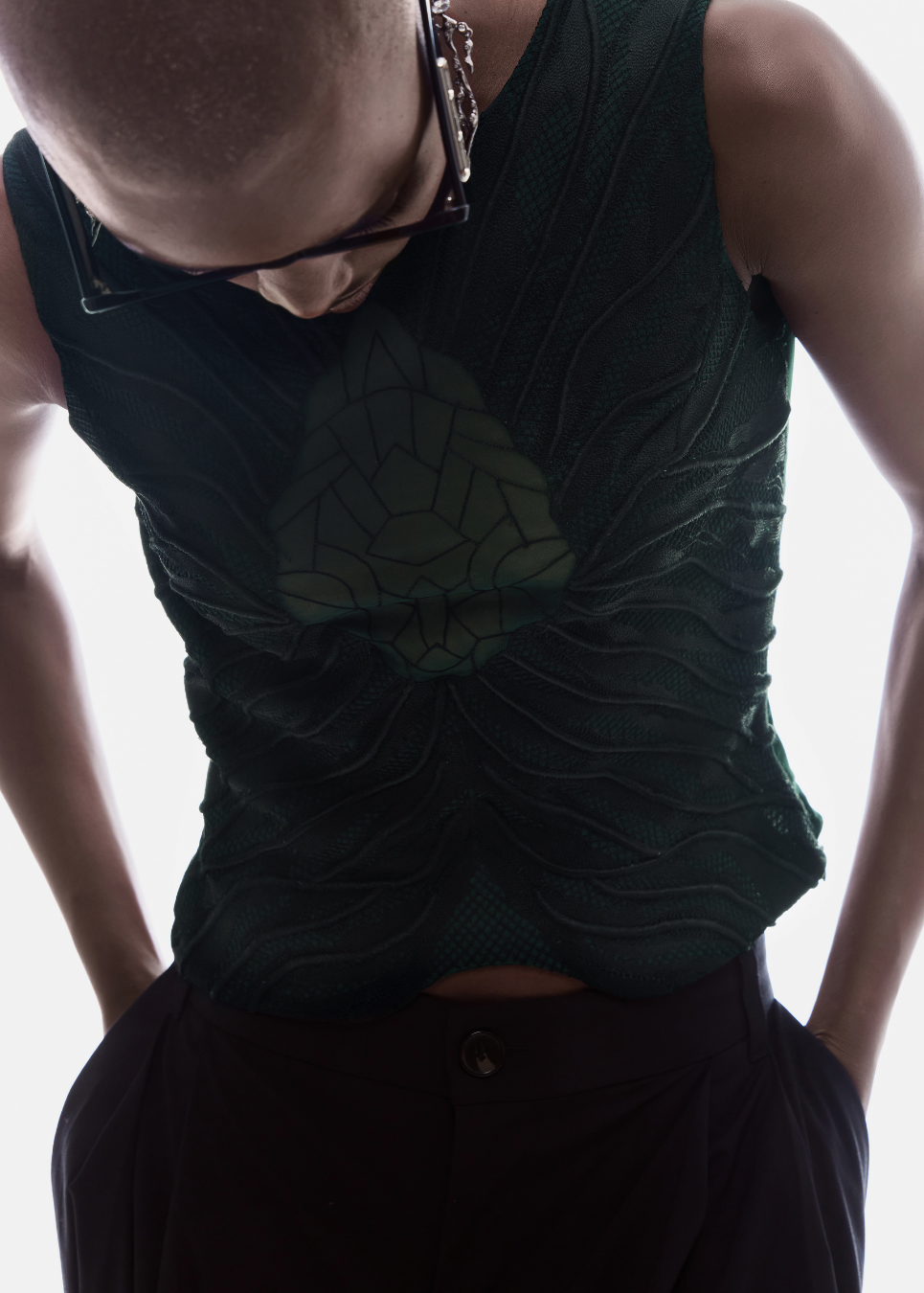 Person wearing a dark green sleeveless top with a textured pattern on a plain background