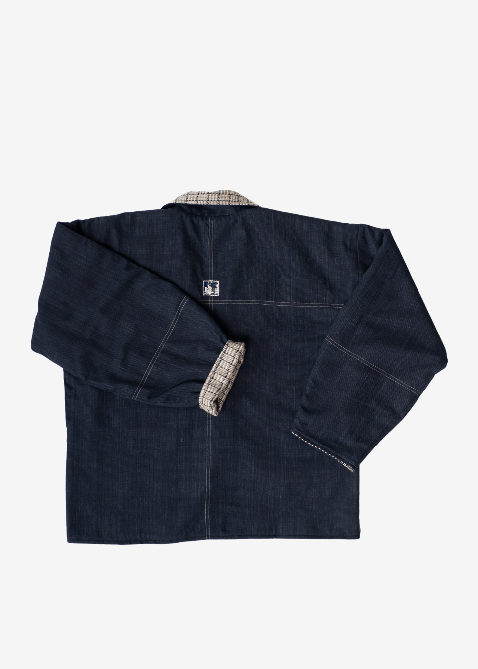 A dark indigo denim jacket with long sleeves and contrast stitching, laid flat against a light gray background. The inner collar and cuff lining feature a beige and white plaid pattern.