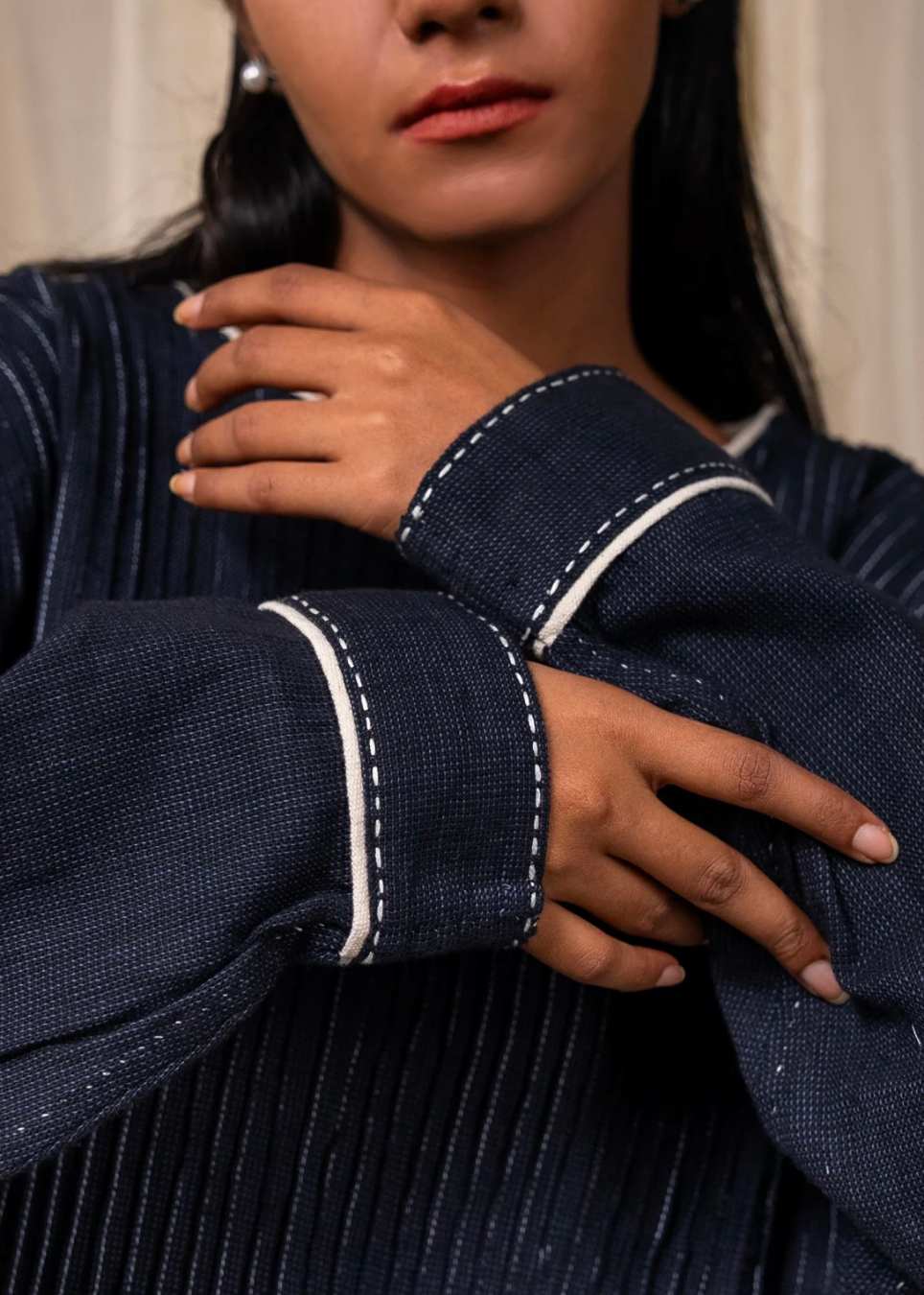 Close-up of a person wearing a dark navy textured shirt with contrasting white stitched trim on the cuffs, showing the hands and lower face.