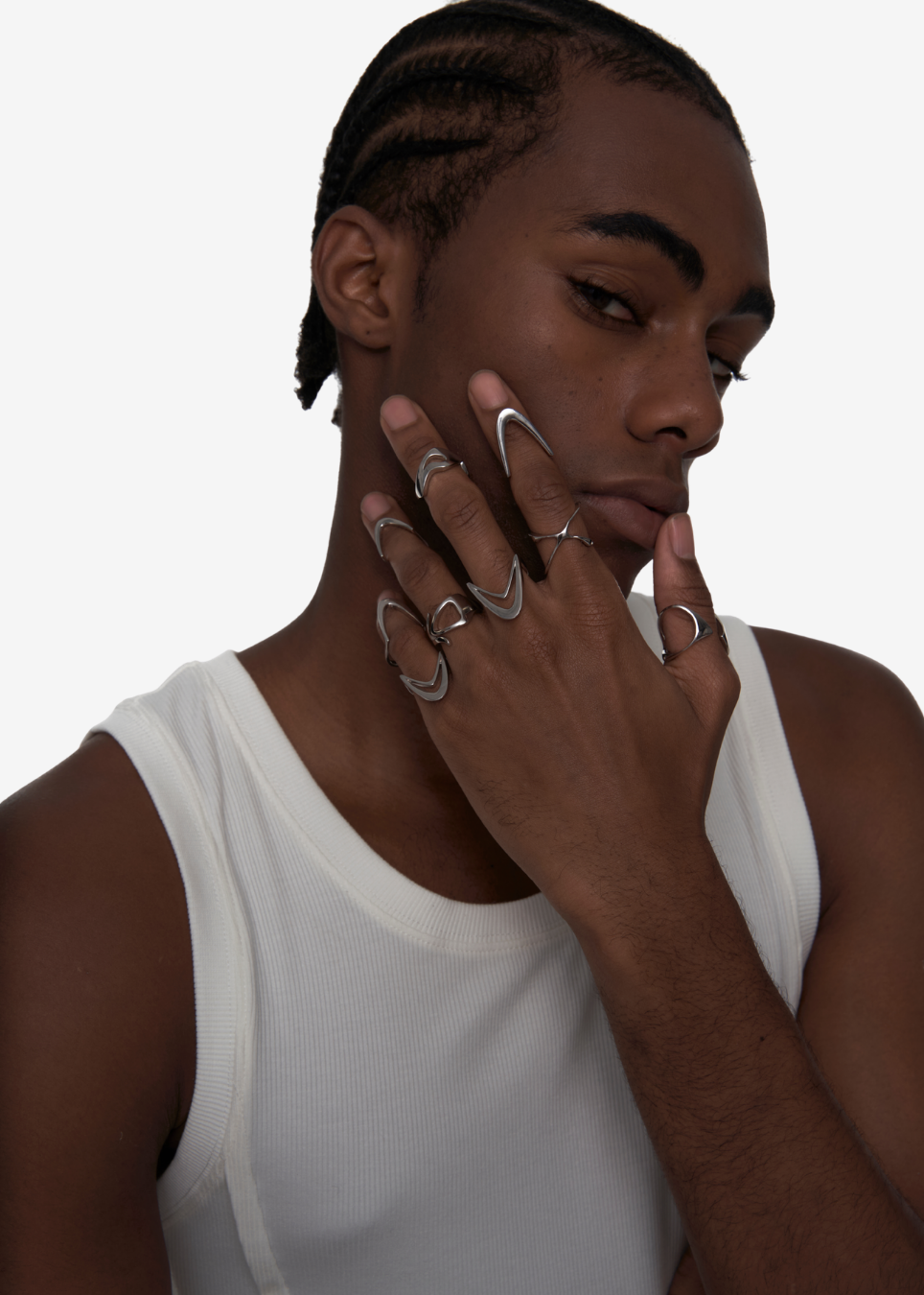 A close-up of a model wearing multiple silver geometric rings on their fingers, with one ring featuring a large circular design. The model is wearing a white ribbed tank top against a plain white background.