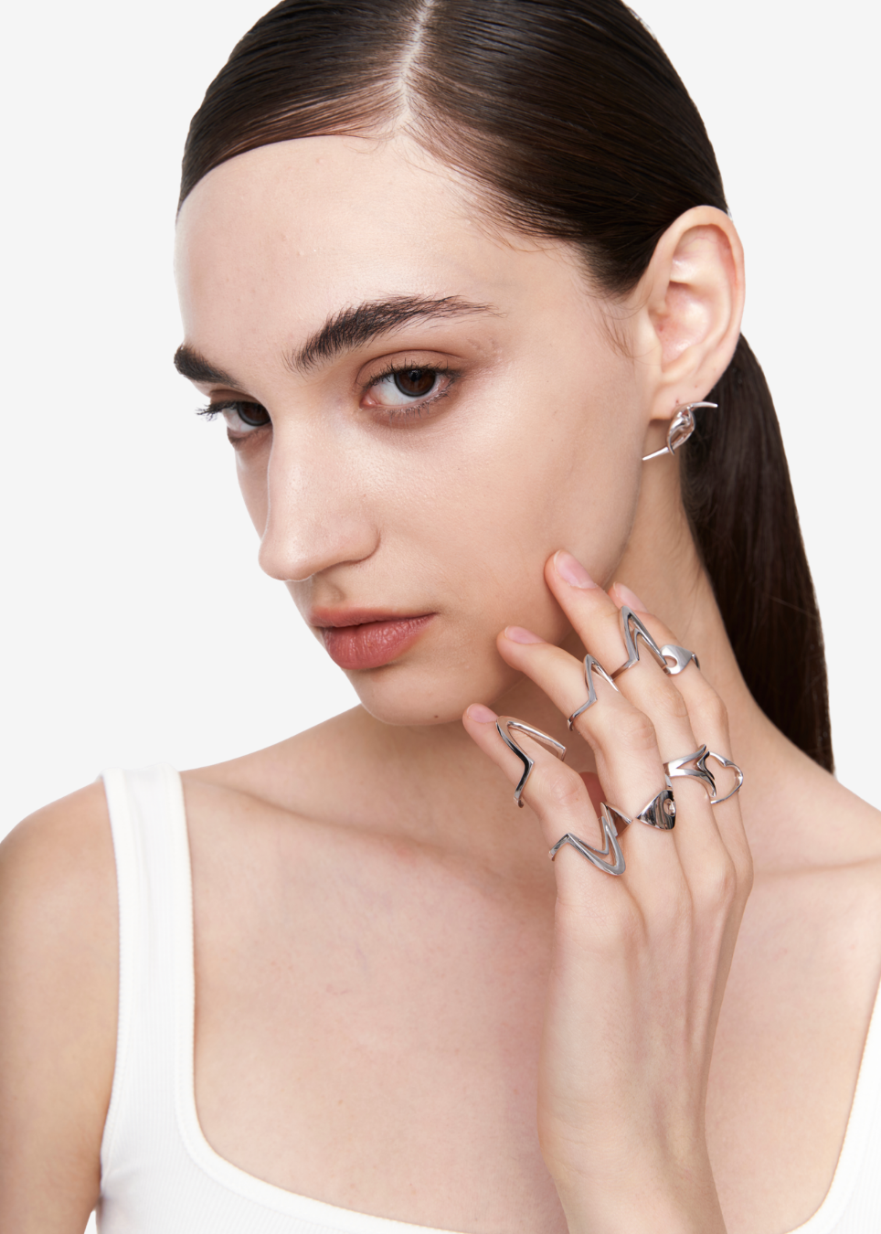 A close-up of a model wearing multiple silver rings with abstract, wavy openwork designs on her fingers and a matching silver earring.