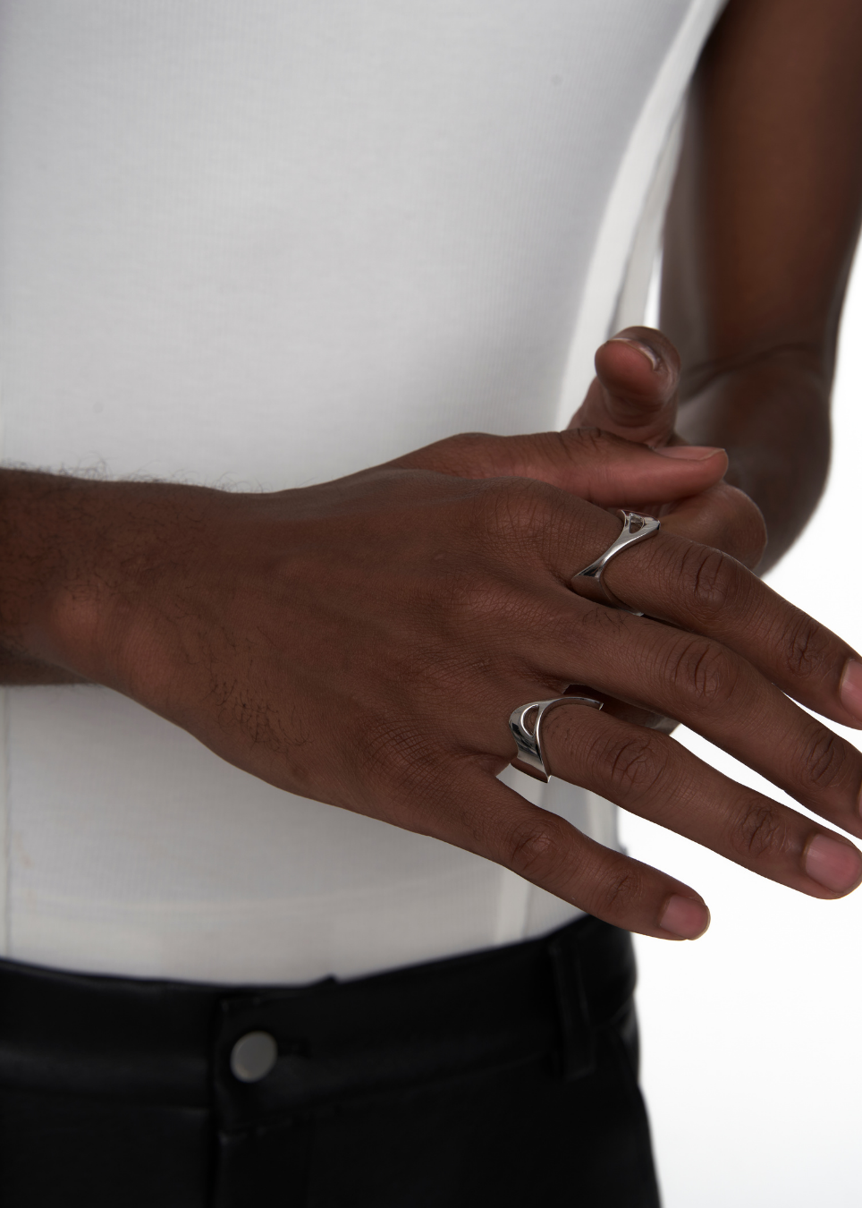 Close-up of a person's hands wearing two silver rings, including a band ring and a double-band ring, styled with a white tank top and black pants.