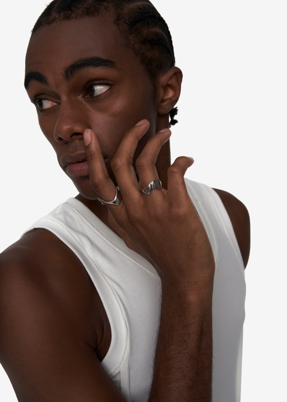 A close-up shot of a man wearing a white ribbed tank top and silver rings on his fingers, set against a plain light gray background.