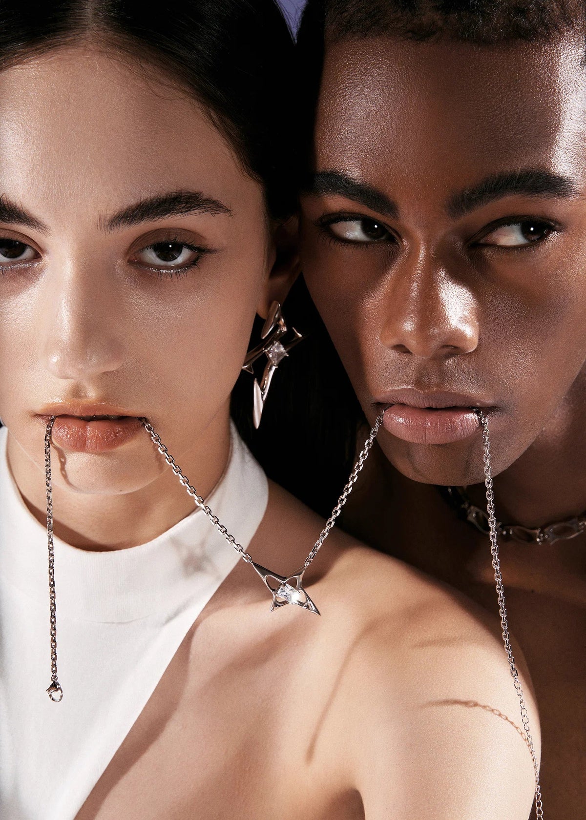 Two models wearing silver chain jewelry with geometric star-shaped earrings and a matching necklace, styled with a white top against a dark background.