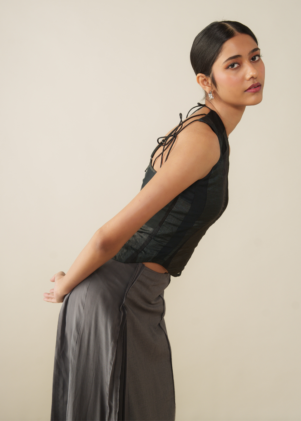 A woman posing in a black sleeveless lace-trimmed top and a dark gray skirt against a plain beige studio background.