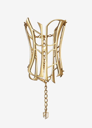 A gold-toned sculptural cuff bracelet with an open, corset-like geometric structure and hanging chains, shown against a plain light gray background.