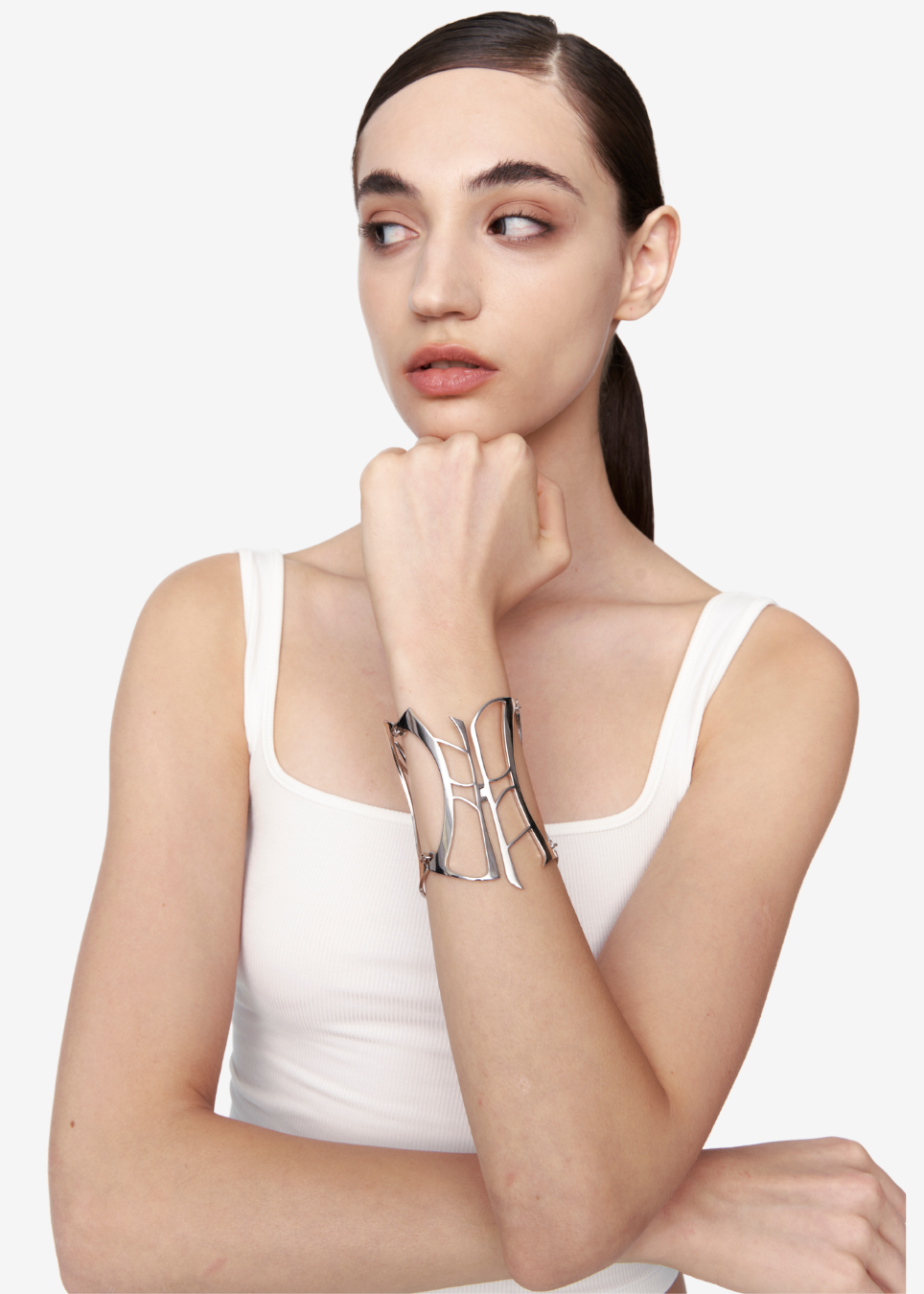 A model wearing a wide, silver-toned metal cuff bracelet with an abstract, openwork design, posed against a clean white background.