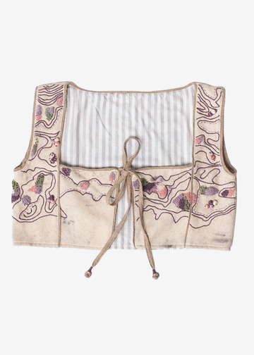 A cropped vest made from distressed denim, featuring a cream-colored body with purple and green floral embroidery, a blue and white striped lining, and a tan drawstring closure.