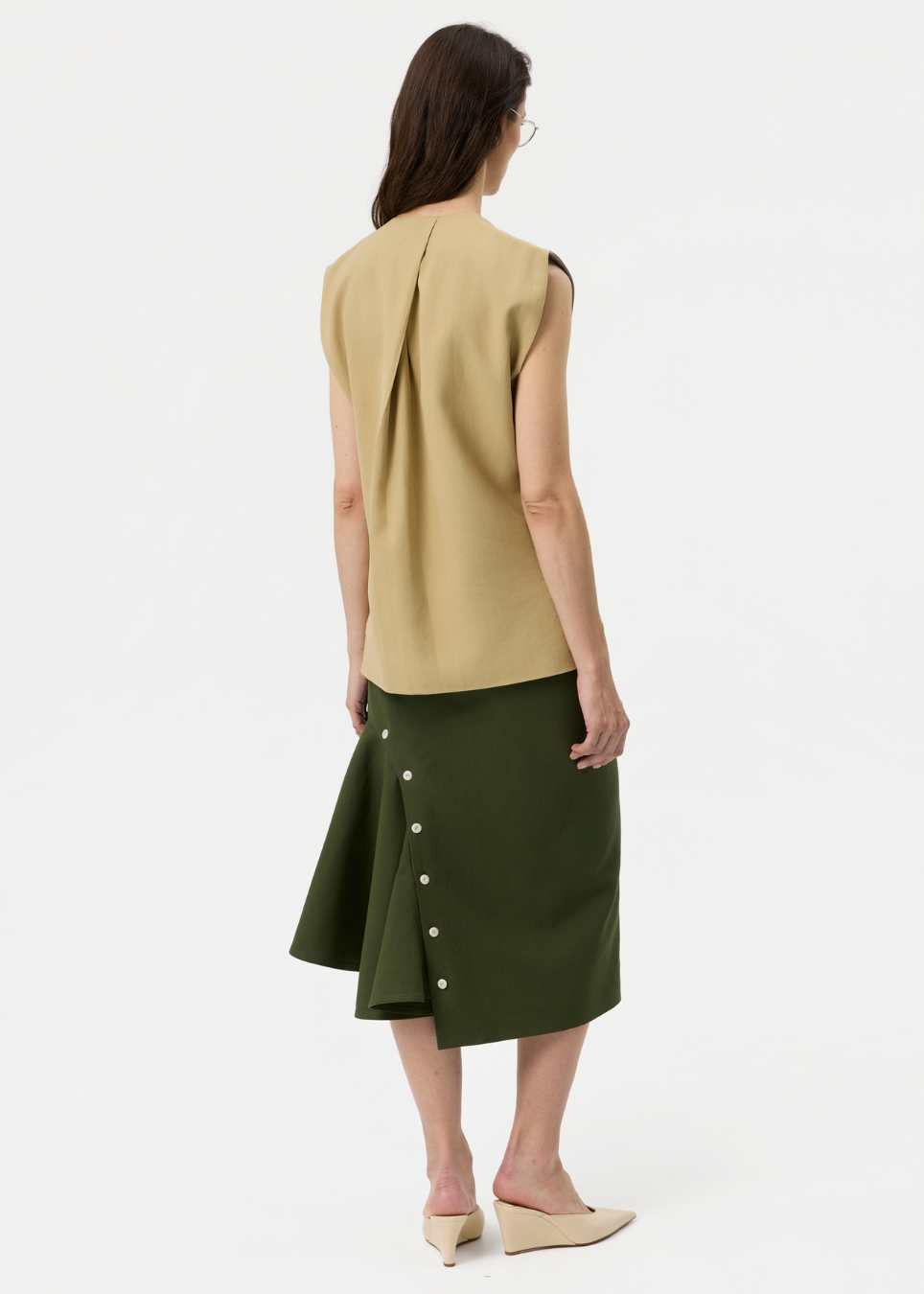 A woman shown from the back wearing a sleeveless beige top and an olive green skirt with decorative buttons down the side, photographed against a plain light background.