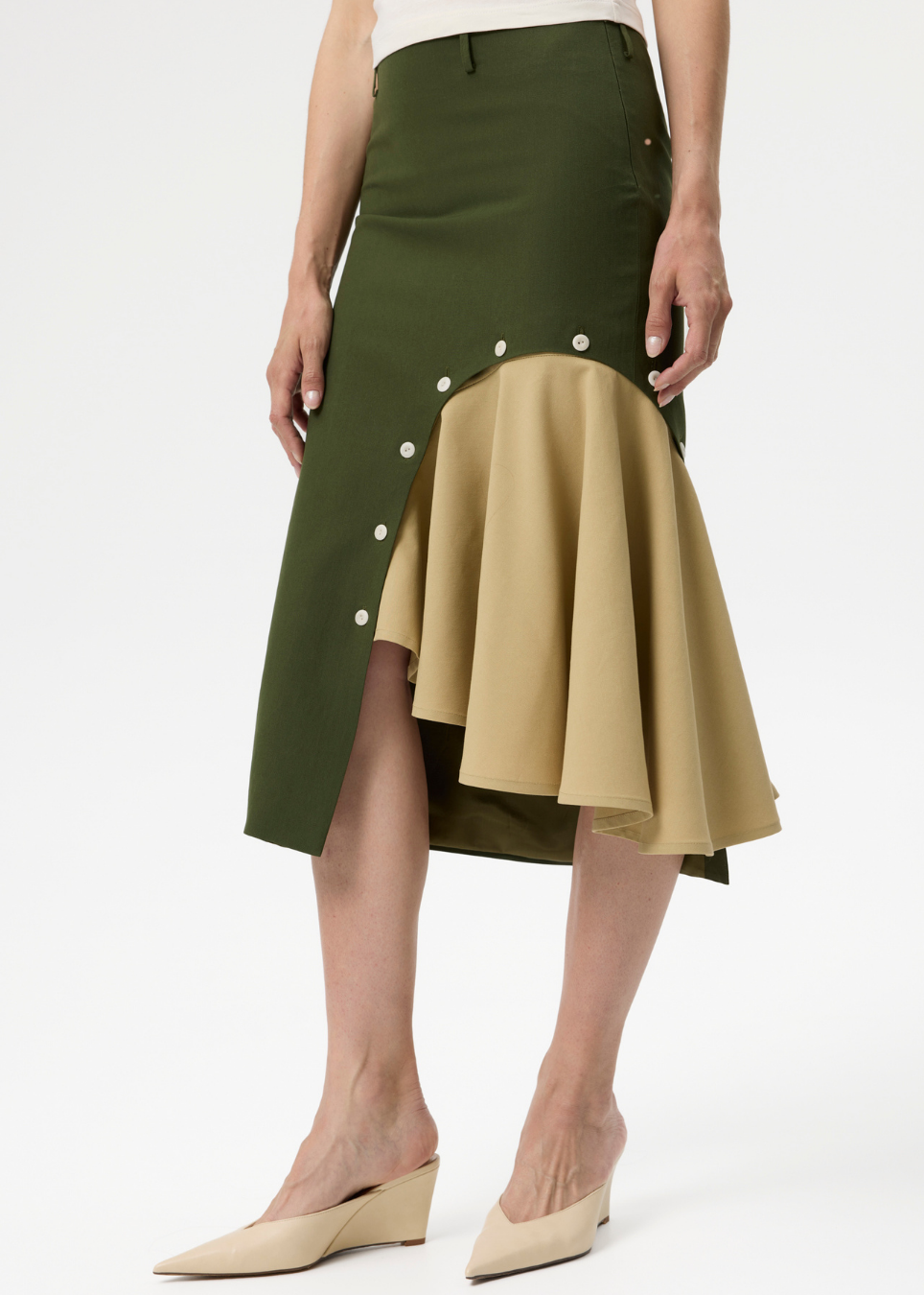 A model wearing a color-blocked midi skirt with an olive green upper section and a beige ruffled lower section, styled with beige wedge mule heels against a white studio background.