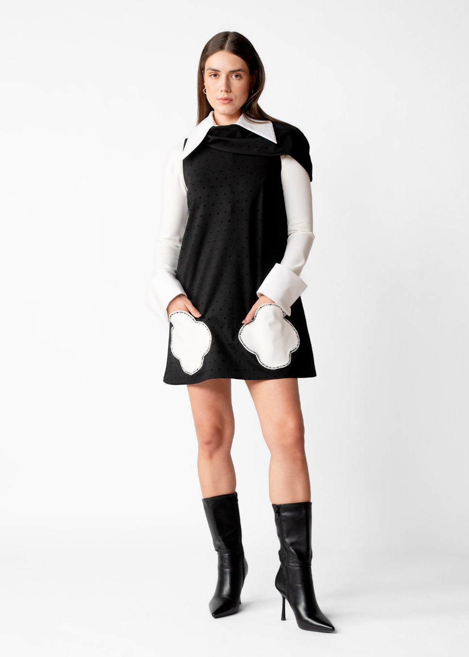 A model wearing a black and white long-sleeve mini dress with white cloud-like patches on the skirt and cuffs, paired with black pointed-toe ankle boots, against a plain white studio background.
