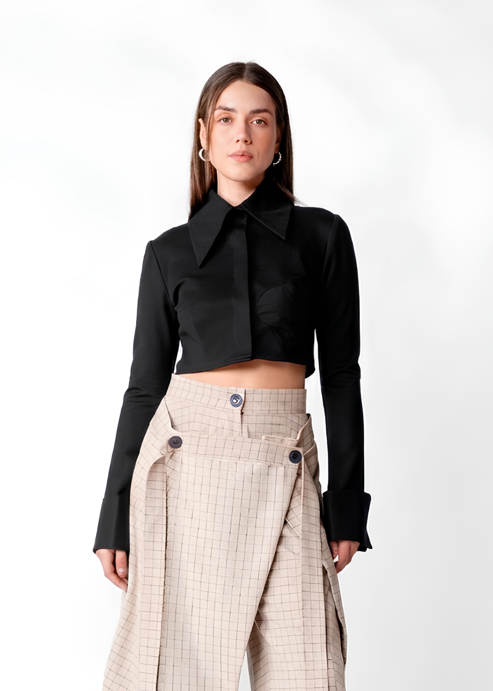 A model wearing a black long-sleeve cropped shirt with a large collar and beige plaid high-waisted trousers, photographed against a plain white studio background.
