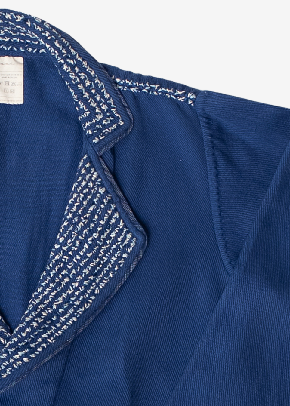 Close-up of a dark blue textured fabric garment, likely a shirt or jacket, featuring a notched lapel with white and blue patterned embroidery along the collar edge.