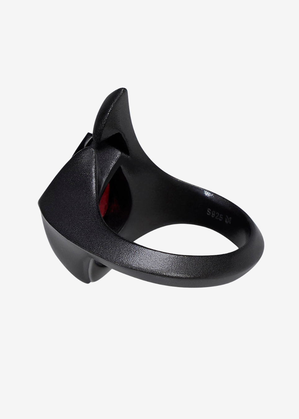 A black sculptural ring with a bold, angular design and a red gemstone visible inside, shown on a light gray background.