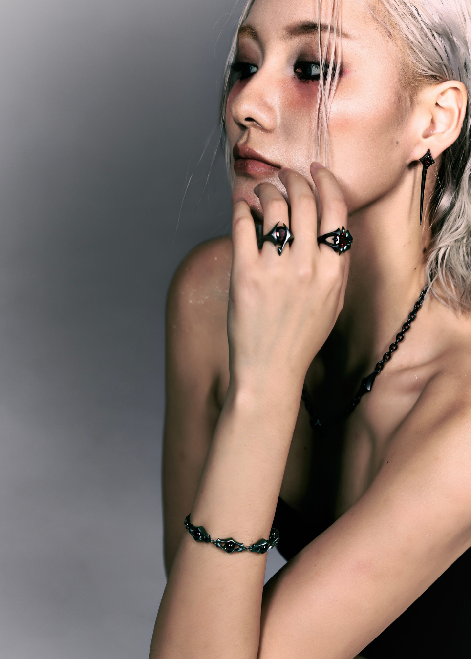 A close-up lifestyle shot of a model with platinum blonde hair wearing gothic jewelry, including black rings, a black beaded necklace, and a black beaded bracelet.