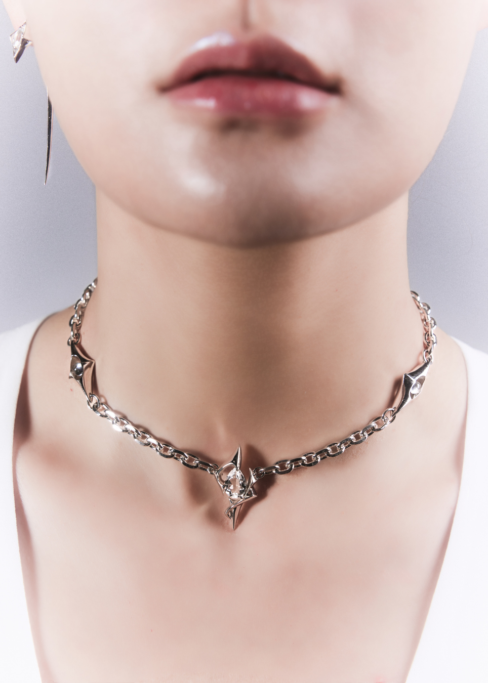 A close-up of a model's neck and lower face wearing a silver-toned chain choker necklace with sharp star and crescent moon details.