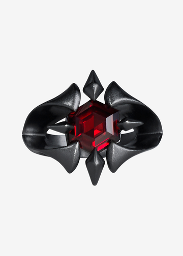 A gothic-style gothic ring featuring a faceted red gemstone in the center, surrounded by a black metal frame with pointed and curved details, set against a plain light gray background.