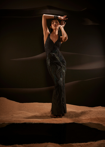 Woman in a dark dress standing on sand with a dark background