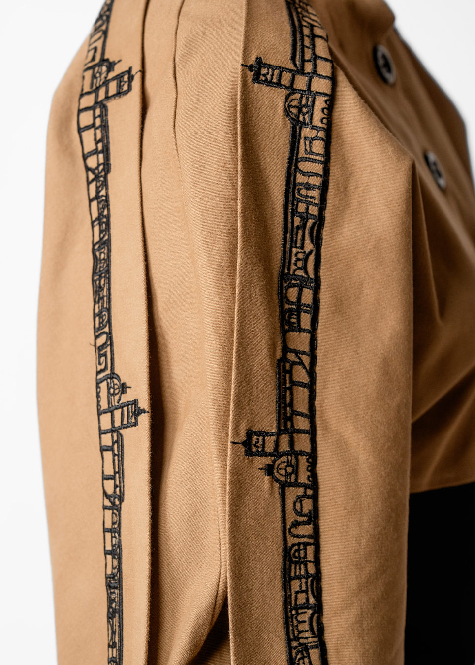 Close-up of a tan or camel-colored garment with black architectural line-art embroidery running vertically along the front panels.
