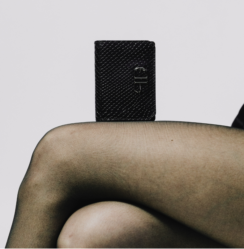 Black textured wallet held by a woman against a light gray background