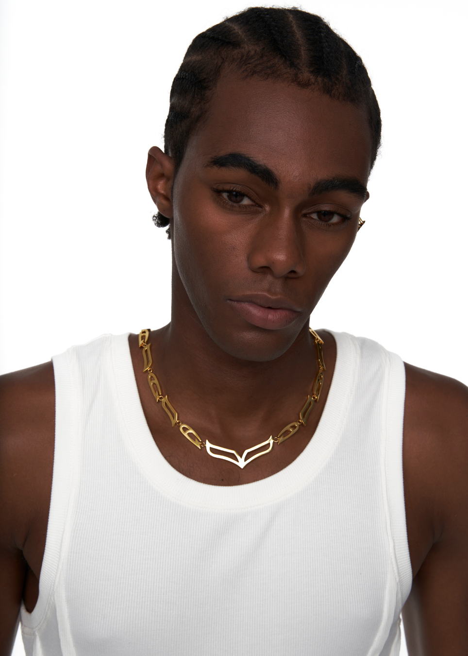 A close-up of a model wearing a gold chain necklace with a geometric, interlocking link design. The model is wearing a white ribbed tank top against a solid white background.