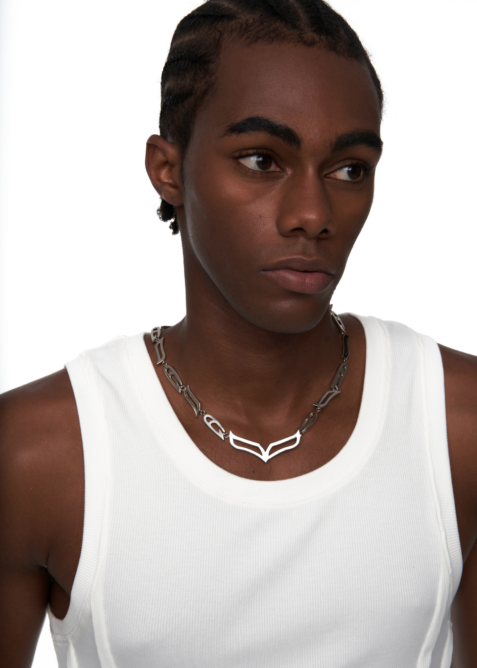 A close-up of a model wearing a silver chain necklace with a geometric V-shaped pendant, paired with a white ribbed tank top against a plain white background.