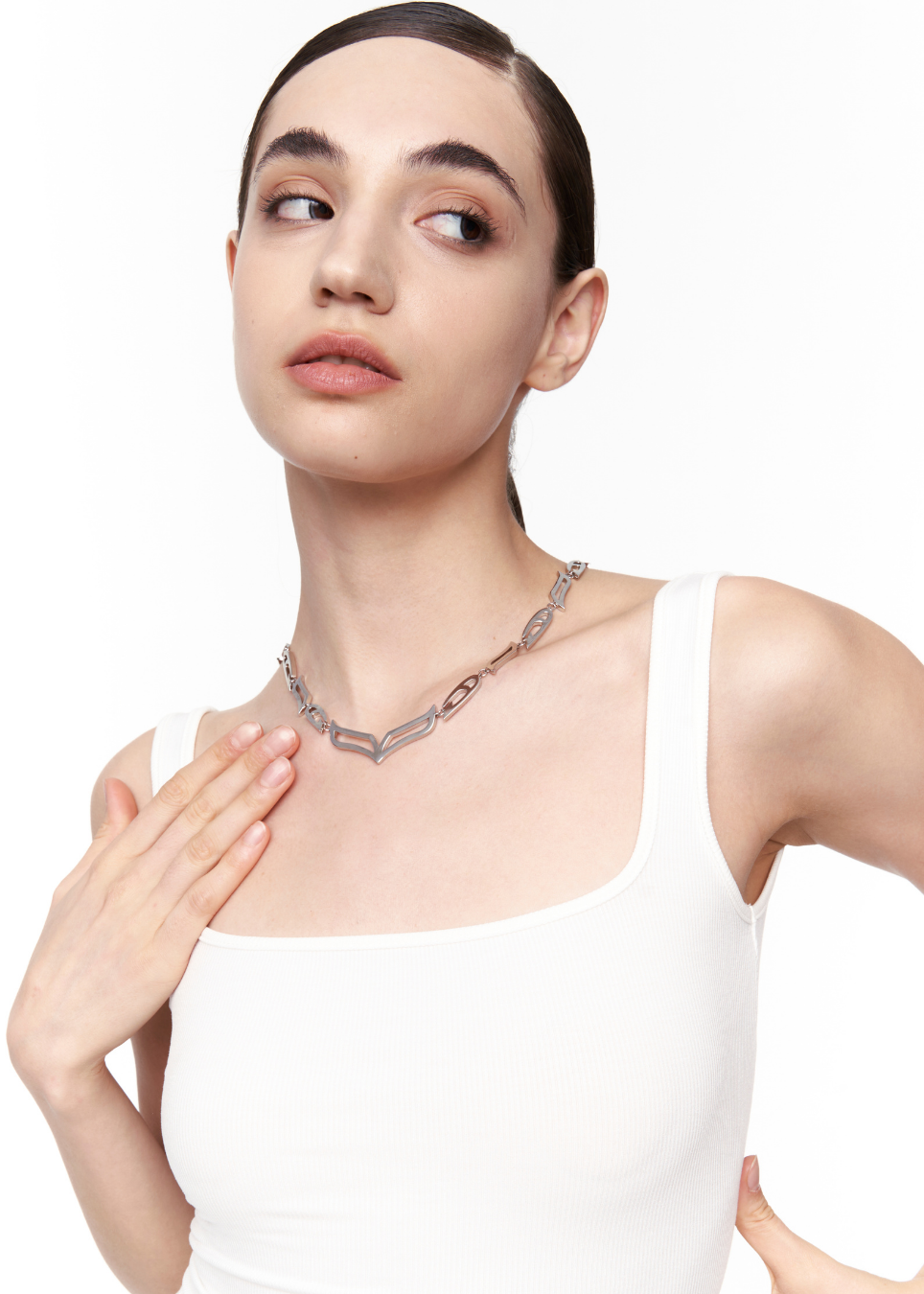 A model wearing a chunky silver chain necklace with geometric links, styled with a white tank top against a plain white background.