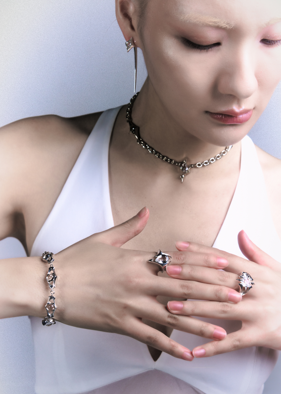 A close-up lifestyle shot of a model wearing a matching silver jewelry set, including a star-shaped ring, a geometric bracelet, and a chain necklace, paired with a white halter top.
