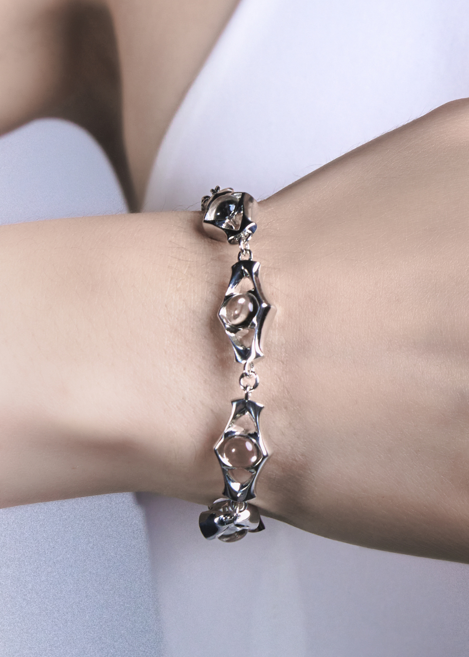 A close-up of a person's wrist wearing a silver-toned bracelet with three elongated, organic-shaped links, each featuring a clear faceted gemstone.