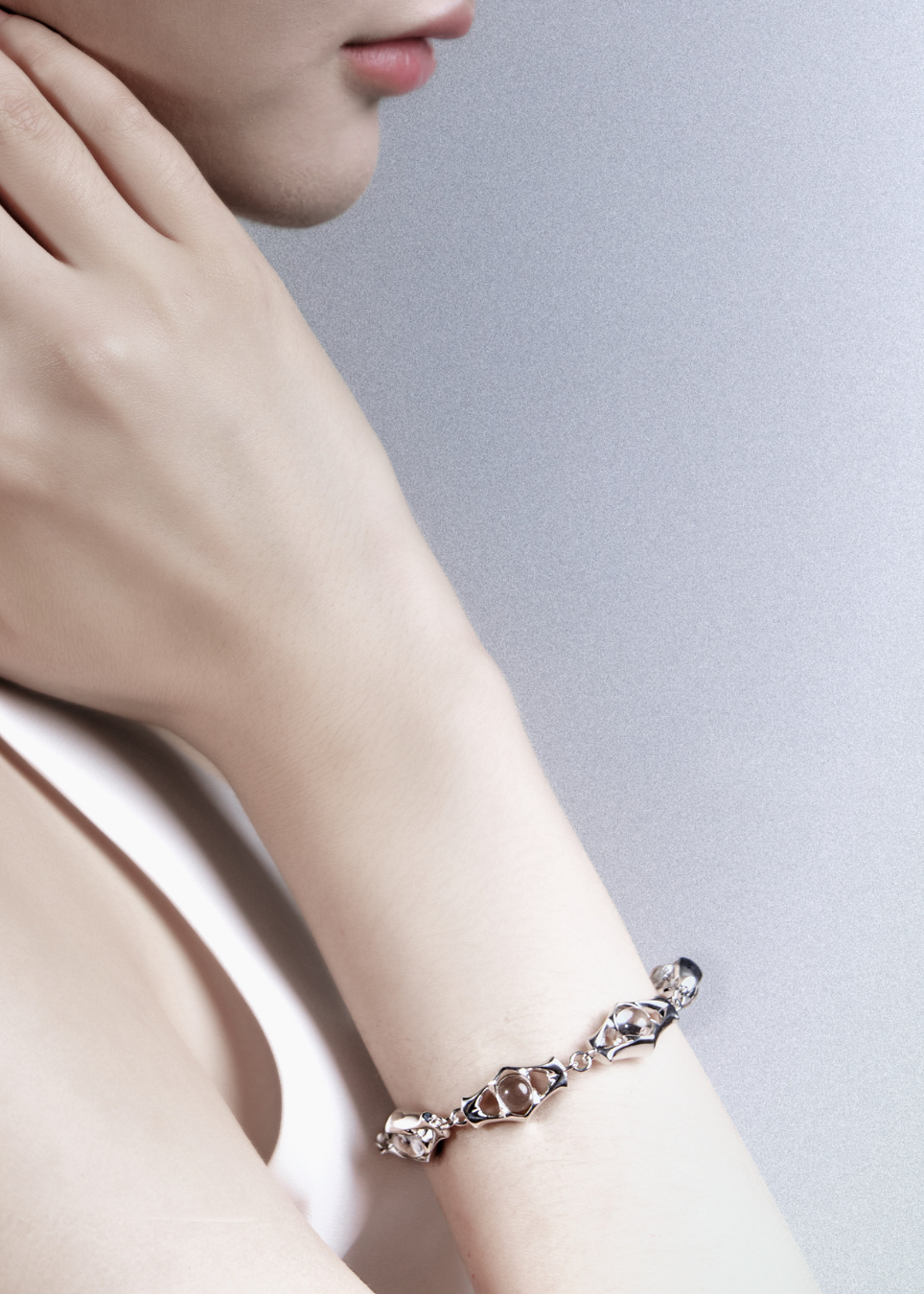 A close-up lifestyle shot of a model's wrist wearing a delicate silver-toned bracelet with heart-shaped links and clear crystals, set against a soft gray background.