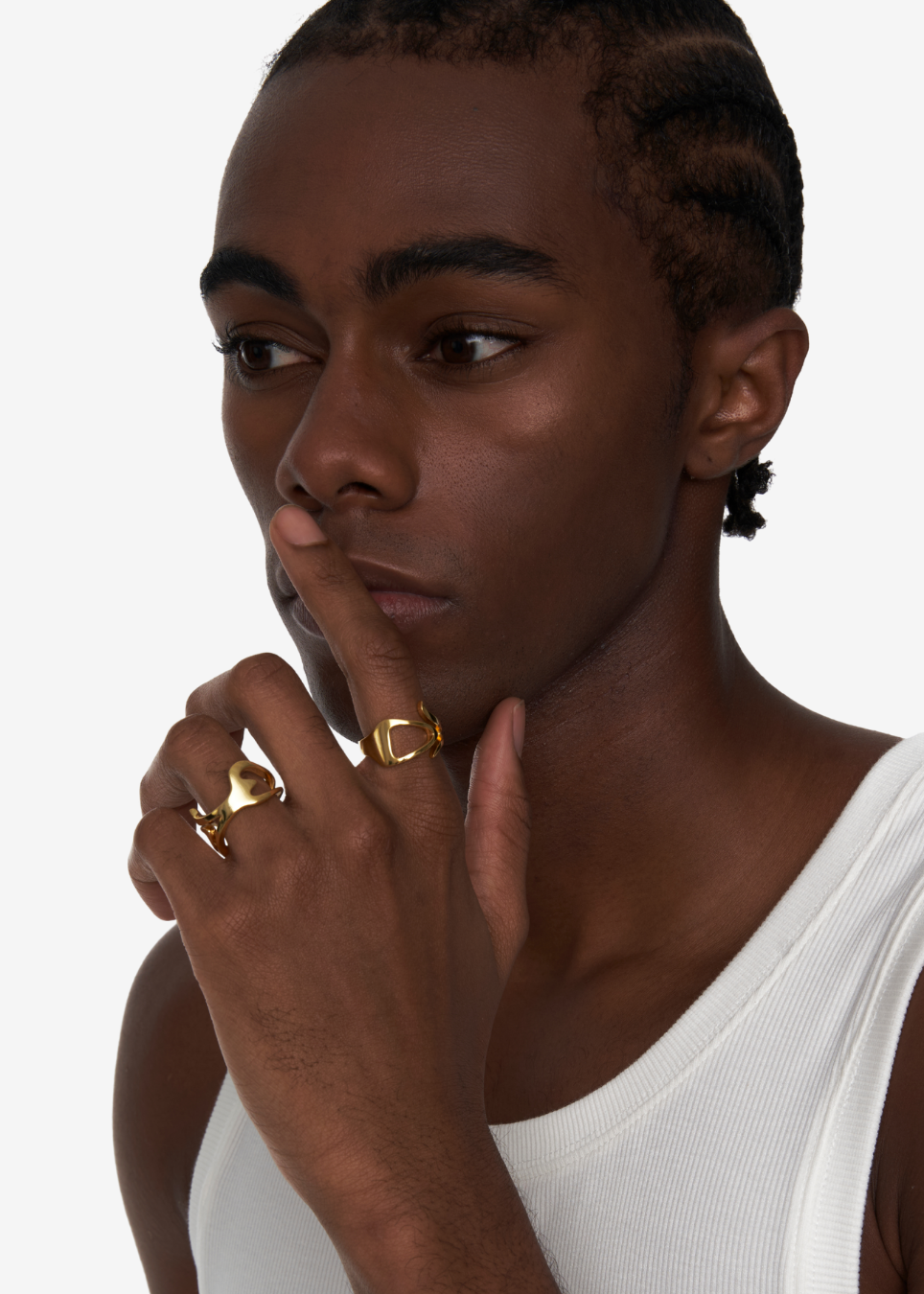 A close-up of a model wearing multiple gold rings on their fingers, including a thick textured band ring and a smaller geometric ring, against a clean white background.
