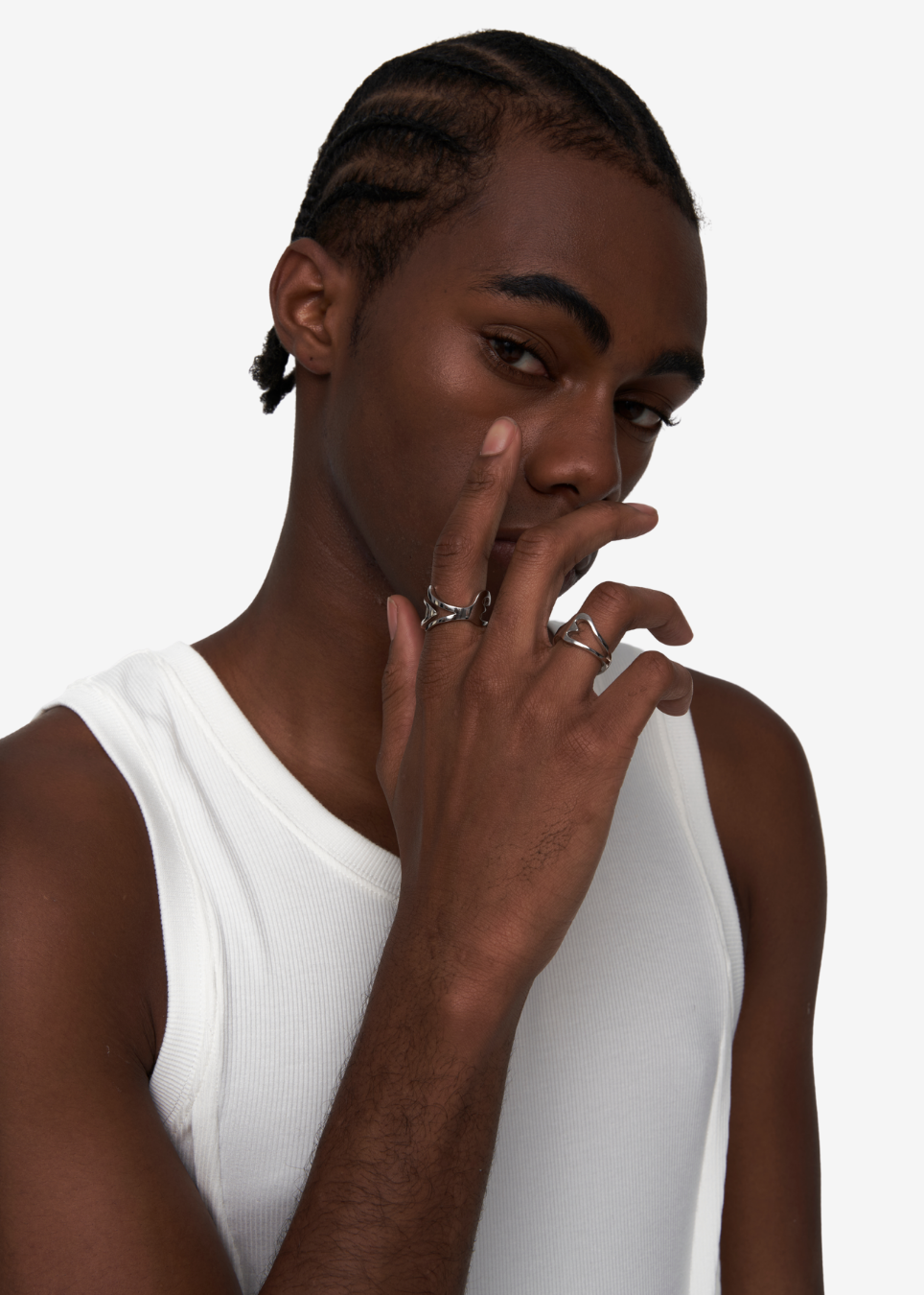 A close-up portrait of a model wearing silver rings on his fingers, dressed in a white ribbed tank top against a plain white background.