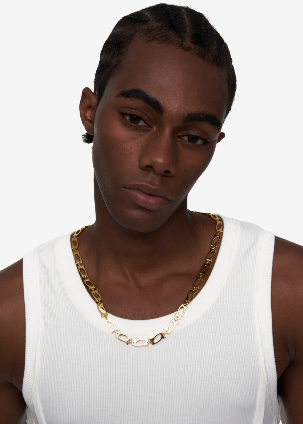A close-up of a man wearing a gold chain necklace with a white ribbed tank top, set against a plain light gray background.