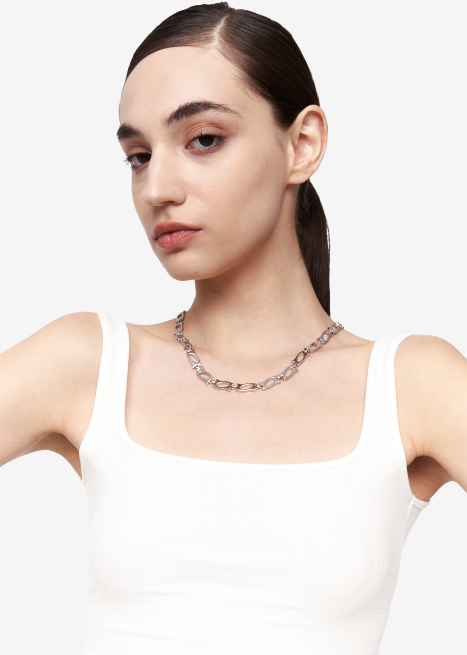 A model with dark hair in a ponytail wearing a white tank top, showcasing a silver-toned chain necklace with alternating clear and rose gold links against a plain light gray background.