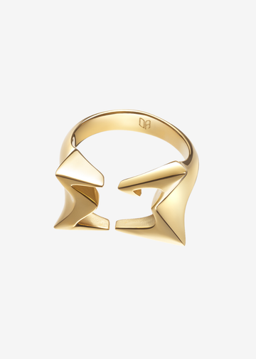 A gold geometric ring with a split band and angular, sculptural elements, shown on a plain light gray background.