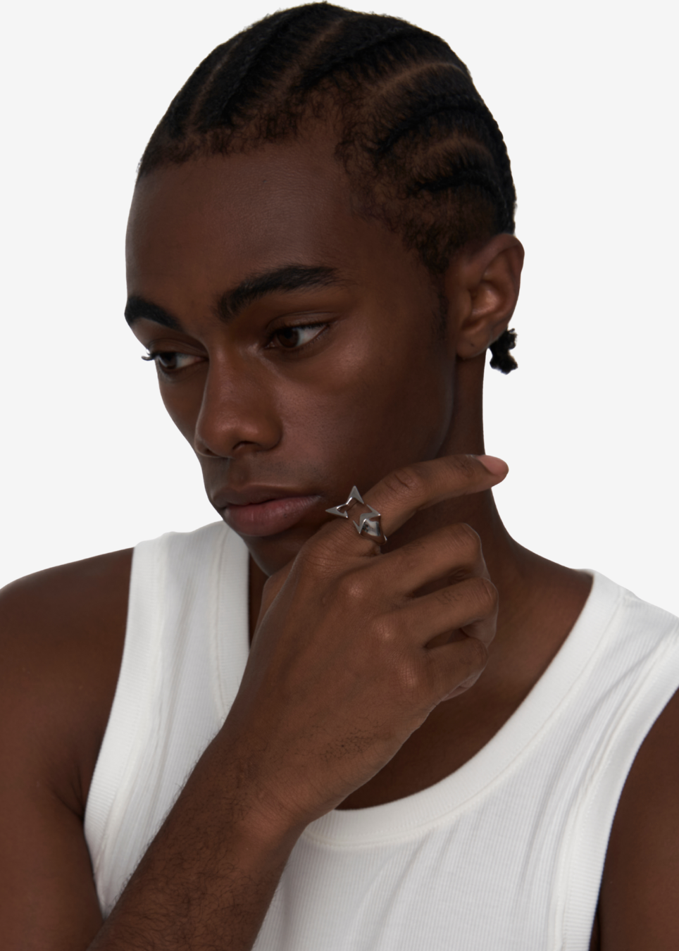 A close-up shot of a man with braided hair wearing a silver geometric ring on his finger, dressed in a white tank top against a plain white background.