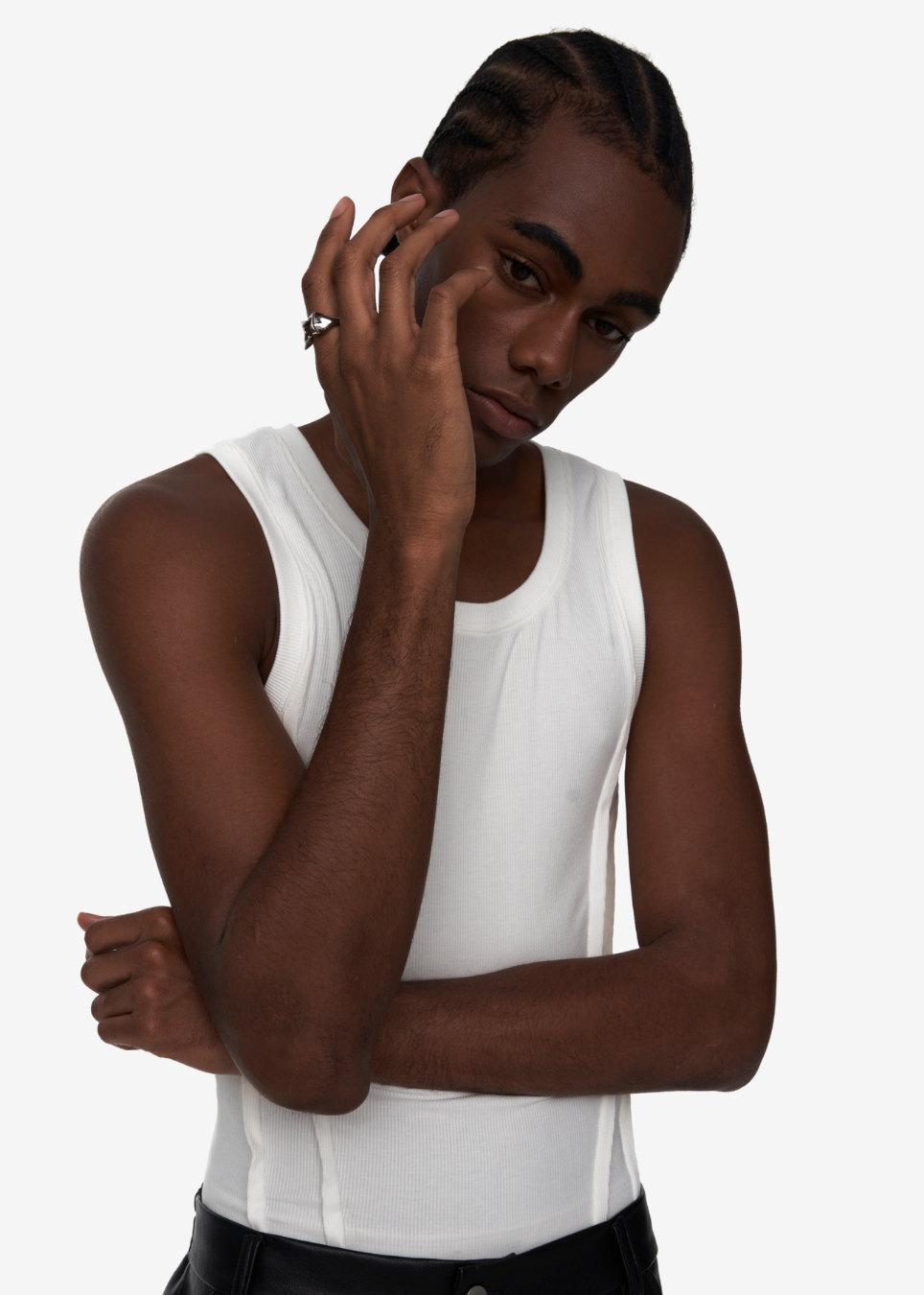 A man wearing a white ribbed tank top, posing with his hand near his face against a plain light gray background.