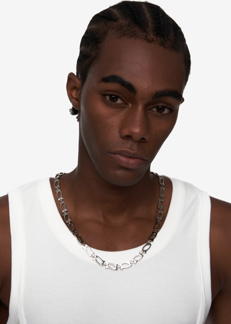 A close-up of a model wearing a chunky silver chain necklace with elongated oval links, paired with a white ribbed tank top against a plain light gray background.