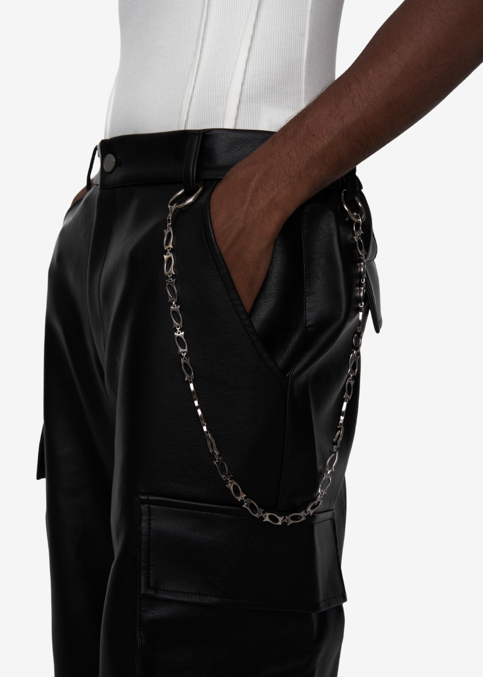 Close-up of a person wearing black faux-leather cargo pants with a silver chain draped from the waistband, paired with a white top against a light gray background.