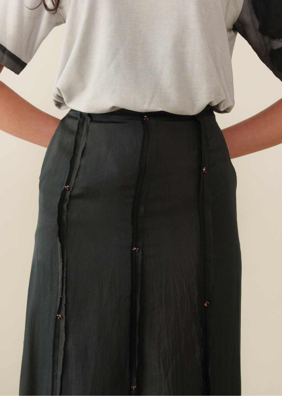 A close-up of a model wearing a dark charcoal gray skirt with vertical seams and small metallic button details, paired with a light gray top.