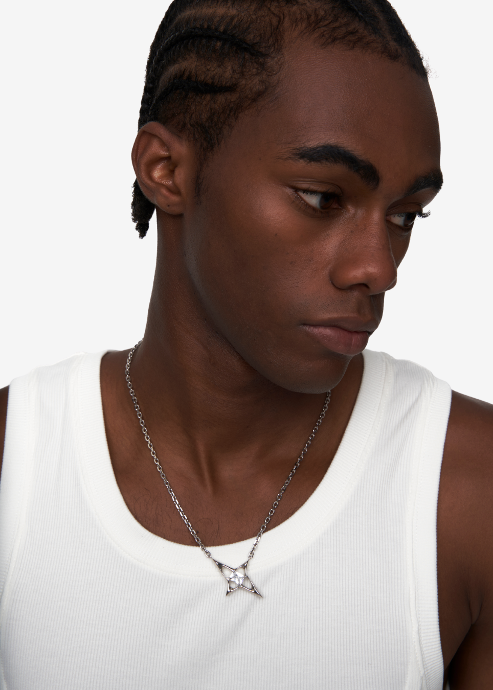 A close-up of a man wearing a silver chain necklace with a geometric star pendant, styled with a white ribbed tank top against a plain white background.