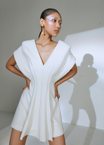 Woman wearing a white dress with a deep neckline against a plain background